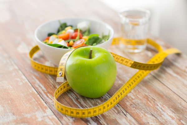 healthy eating, dieting, slimming and weigh loss concept - close up of green apple, measuring tape and salad