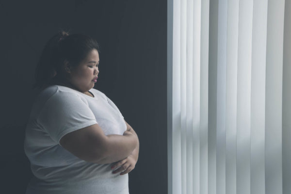 Picture of lonely obese woman looks sad while standing near the window