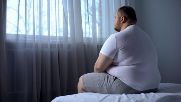 Sad heavy man sitting on bed at home, health problem, depression, insecurities